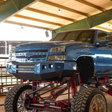 2005-2007 chevy truck with oversized off-road tires and a custom red frame, shown in a warehouse setting.
