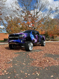 A truck with a custom purple and black grille insert, parked in a lot with fall leaves on the ground.