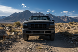 Front view of a dark gray Ford pickup truck in a workshop, showing the front grille, headlights, and lower bumper area.